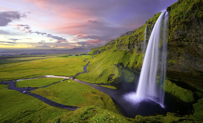 A beautiful landscape with green plains and a tall waterfall pouring from a moss-covered rock face. Original public domain image from Wikimedia Commons